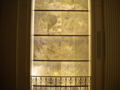 Von hinten beleuchtete Marmorwand mit verziertem Metallgeländer davor.
