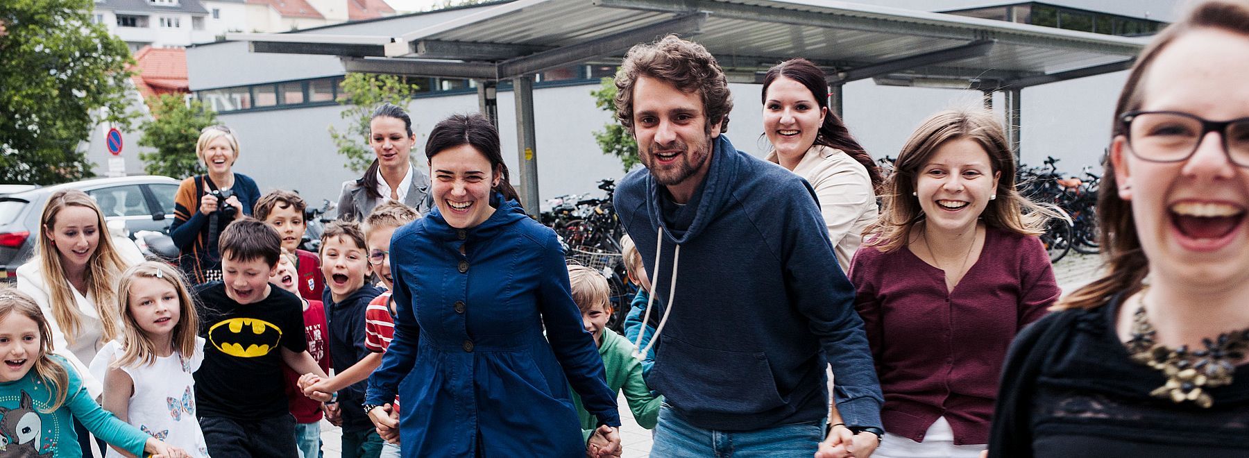 Eine Gruppe lächelnder Erwachsener und Kinder, die Händchen halten und im Freien herumlaufen.